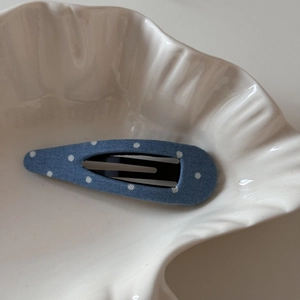 Gros plan détaillé d'une pince à cheveux en denim bleu à pois sur une assiette blanche
