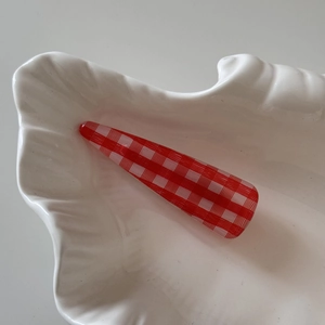 Close-up of a red gingham pattern hair clip placed on a white shell-shaped tray
