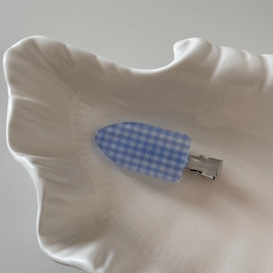 Detail of blue and white gingham hair clip on a shell ceramic plate with soft shadows