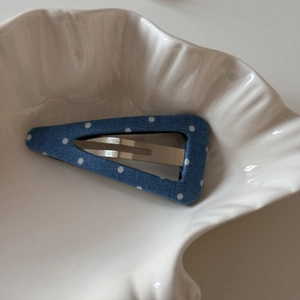 Détail d'une pince à cheveux triangulaire bleue à pois sur une assiette en céramique