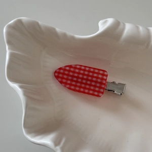 Detail view of a vintage red and white plaid hair clip on a white shell tray