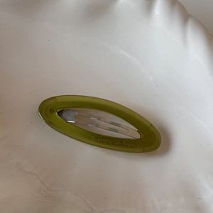 Close-up of olive green oval acetate hair clip with silver metal barrette detail