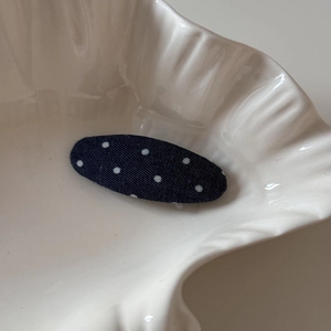 Gros plan d'une pince à cheveux ovale en denim à pois bleus sur un plateau blanc