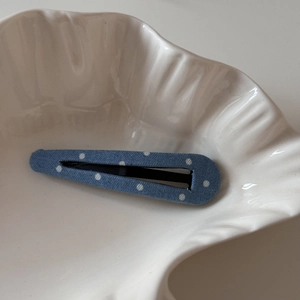 Détail d'une pince à cheveux BB en tissu bleu à pois sur une coupelle coquillage