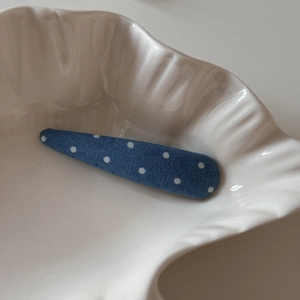 Détail d'une pince à cheveux en jean bleu à pois dans un bol en céramique blanc