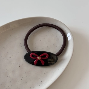 Détail d'un élastique à cheveux marron avec un nœud rouge et l'inscription France Handmade