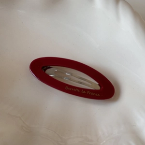 Detailed close-up of a vintage red oval acetate hair clip featuring gold lettering on porcelain