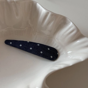 Détail d'une barrette en tissu bleu marine à pois blancs sur un plat en céramique blanc