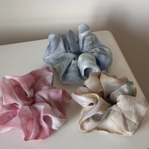 Close-up of three iridescent organza scrunchies in pink, blue, and champagne colors