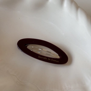 Detail view of dark red acetate oval hair clip with gold lettering on a white tray