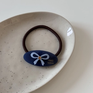 Détail d'élastique en acétate bleu avec nœud et strass sur une assiette en céramique
