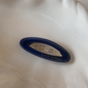 Macro detail of oval acetate hair clip in dark blue with golden lettering text