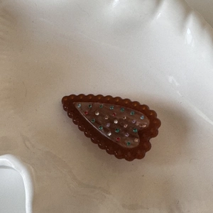 Détail d'une pince à cheveux marron en forme de cœur avec strass colorés et bords ondulés