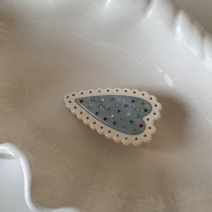 Détail de la pince à cheveux en forme de cœur avec bords festonnés et strass colorés