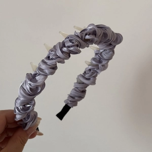 Detail showing hand holding purple satin headband with decorative white horn accents