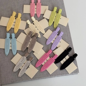 Close-up of ten pairs of colorful metal hair clips arranged on a textured grey fabric surface