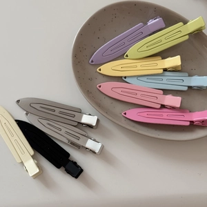 Flat lay of colorful metal duckbill hair clips on a minimalist ceramic plate