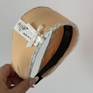 Close-up of orange fabric headband with lace checkered trim, white bow, and pearl detail