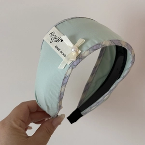 Detail of mint green padded headband with silk bow, pearl accent and woven Korean label