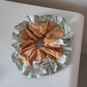 Detail of sweet plaid scrunchie featuring orange fabric, lace trim, and pearl bow detail