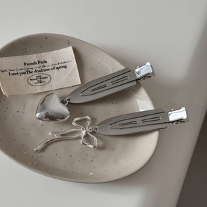Details von silbernen Haarspangen mit Herz und Schleife auf einem beigen Keramikteller
