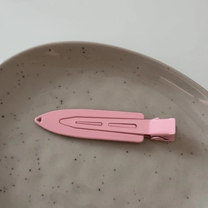 Close-up of a pink matte metal duckbill hair clip with hollow lines on a ceramic dish