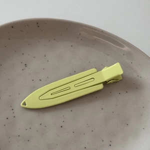 Macro detail of a neon yellow matte duckbill hair clip on a minimalist ceramic tray