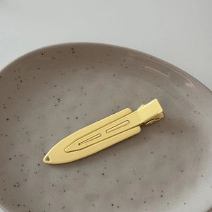 Detailed side view of matte pale yellow minimalist metal alligator hair clip on ceramic plate