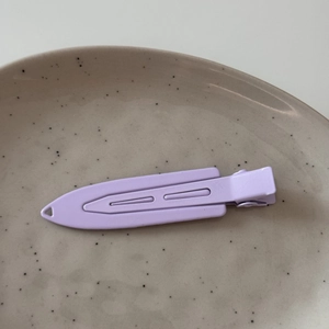 Detail view of a matte purple metal duckbill hair clip on a gray ceramic plate