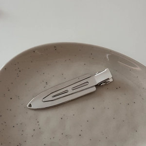 Polished silver metal duckbill hair clip with sleek pointed design on a ceramic tray