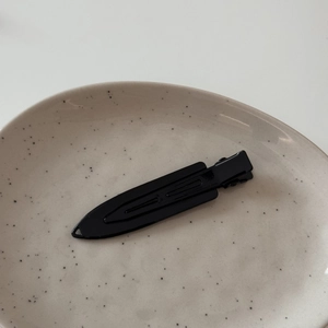 Macro shot of a sleek black metal duckbill hair clip on a textured ceramic plate