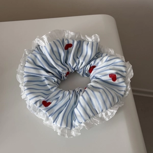 Détail de broderie cœurs rouges sur chouchou rayé bleu avec bord en dentelle