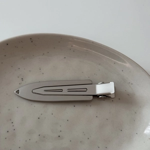 Sleek silver metal hair clip with geometric lines on a ceramic tray minimalist style
