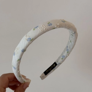 Détail d'un serre-tête blanc rembourré avec broderies florales bleues et doublure antidérapante