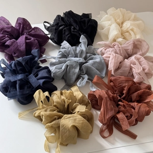 Flat lay of eight colorful large chiffon scrunchies with pleated texture for hair
