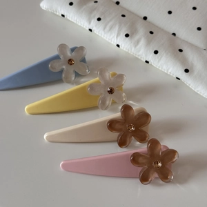 Détail de quatre pinces à cheveux fleurs en résine bleue, jaune, crème et rose avec strass