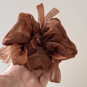 Macro shot of oversized pleated caramel chiffon scrunchie showing semi-transparent fabric texture