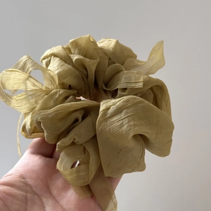Detail of oversized ruffled chiffon scrunchie in olive yellow held in hand