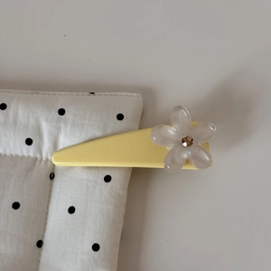 Détail d'une pince à cheveux jaune triangulaire avec fleur en résine et petit cristal