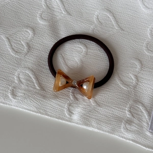 Close-up of amber acetate bow hair tie featuring inlaid pearls and sparkling rhinestone detail