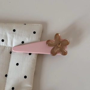Détail d'une pince à cheveux rose avec fleur marron et paillettes sur un tissu à pois