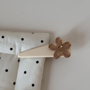 Gros plan d'une pince à cheveux crème avec fleur en résine café et strass central