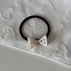 Close-up of cream acetate bow hair tie with rhinestone and faux pearls on brown elastic band