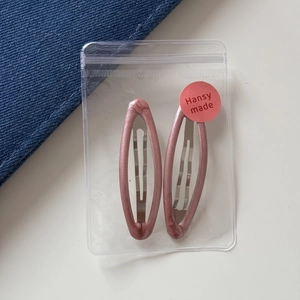 Detail of two glitter pink oval BB hair clips inside a clear plastic bag on white background