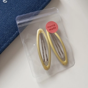 Detail view of two glitter resin snap hair clips in transparent packaging on denim