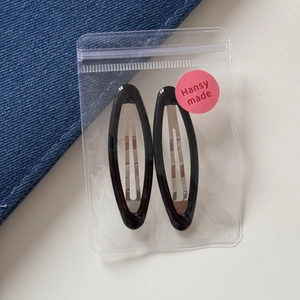 Set of two black oval hair clips in transparent packaging with metallic base clips