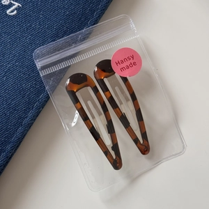 Detail view of two tortoise shell teardrop hair clips in transparent brand packaging