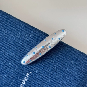Gros plan d'une pince à cheveux argentée à pois bleu clair sur un fond en denim bleu