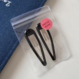 Close-up of two black glossy teardrop BB hair clips in a frosted zipper pouch