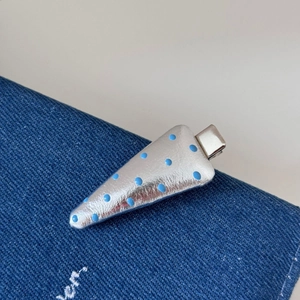 Détail d'une pince à cheveux triangulaire argentée avec pois bleus sur denim